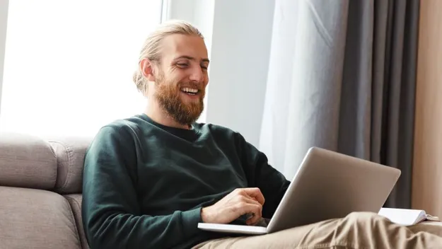 Ein Mann sitzt auf einem Sofa. Als kostenbewusster Altersvorsorgesparer vergleicht er auf seinem Laptop die Konditionen verschiedener Anbieter.
