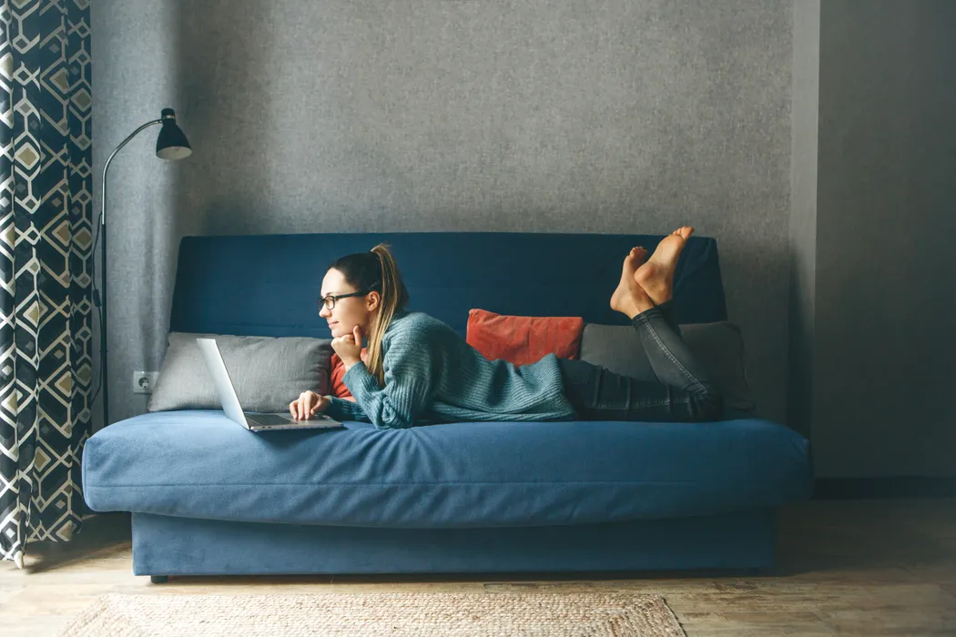 Junge Frau auf einem Sofa ließt Informationen zur Erwerbsunfähigkeitsversicherung auf dem Laptop