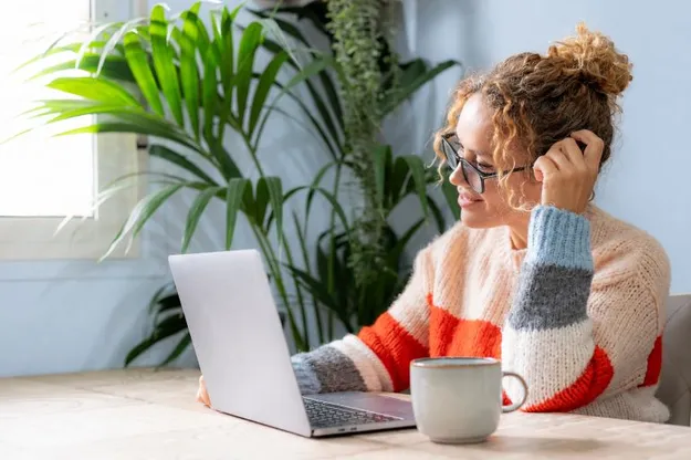 Eine junge Frau sitzt in einem Raum an einem Tisch und liest sich Ratgeber zur Altersvorsorge am Laptop durch.