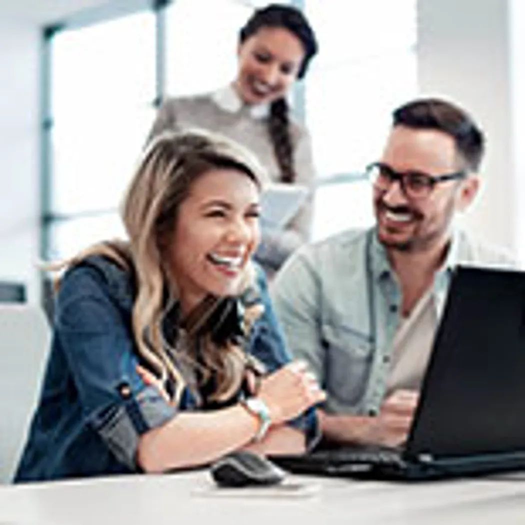 Risikolebensversicherung: Geschäftspartner In einem modernen Büro arbeiten zwei Geschäftspartner gemeinsam an einem Laptop. Sie diskutieren konzentriert über Details einer Risikolebensversicherung, während im Hintergrund eine Person Notizen macht.