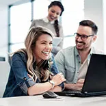 In einem modernen Büro arbeiten zwei Geschäftspartner gemeinsam an einem Laptop. Sie diskutieren konzentriert über Details einer Risikolebensversicherung, während im Hintergrund eine Person Notizen macht.