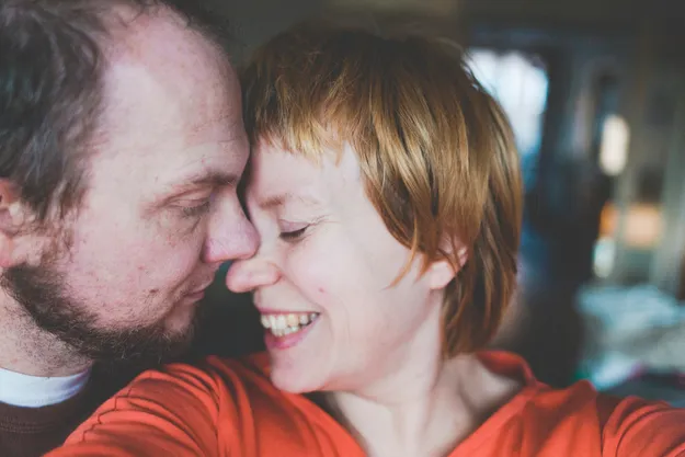 Ein glückliches Paar steht in einem gemütlichen Raum. Beide tragen lässige Kleidung. Die Szene vermittelt ein Gefühl von Sicherheit, das durch eine Risikolebensversicherung unterstützt werden könnte.