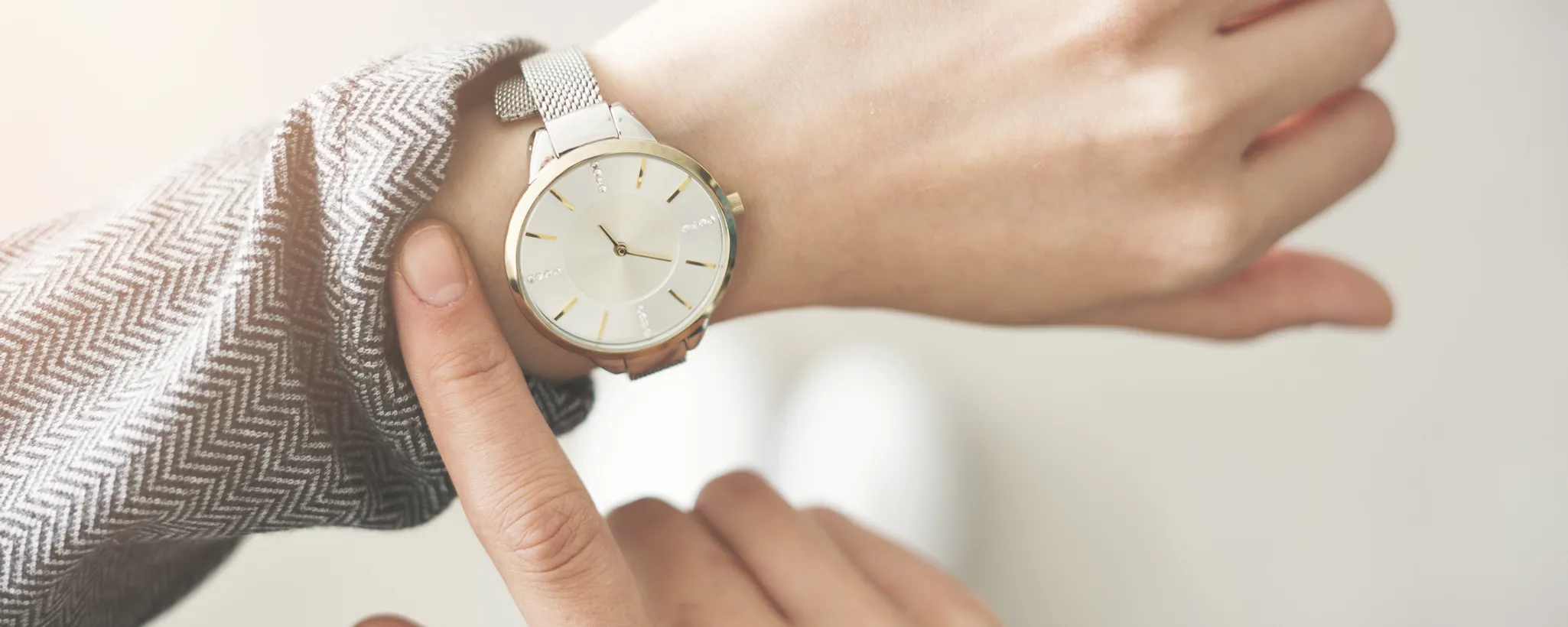 Eine Person trägt eine elegante Armbanduhr und zeigt darauf, was den Faktor Arbeitszeit symbolisiert. Der Fokus liegt auf der Uhr, die in der Arbeit wichtig ist.