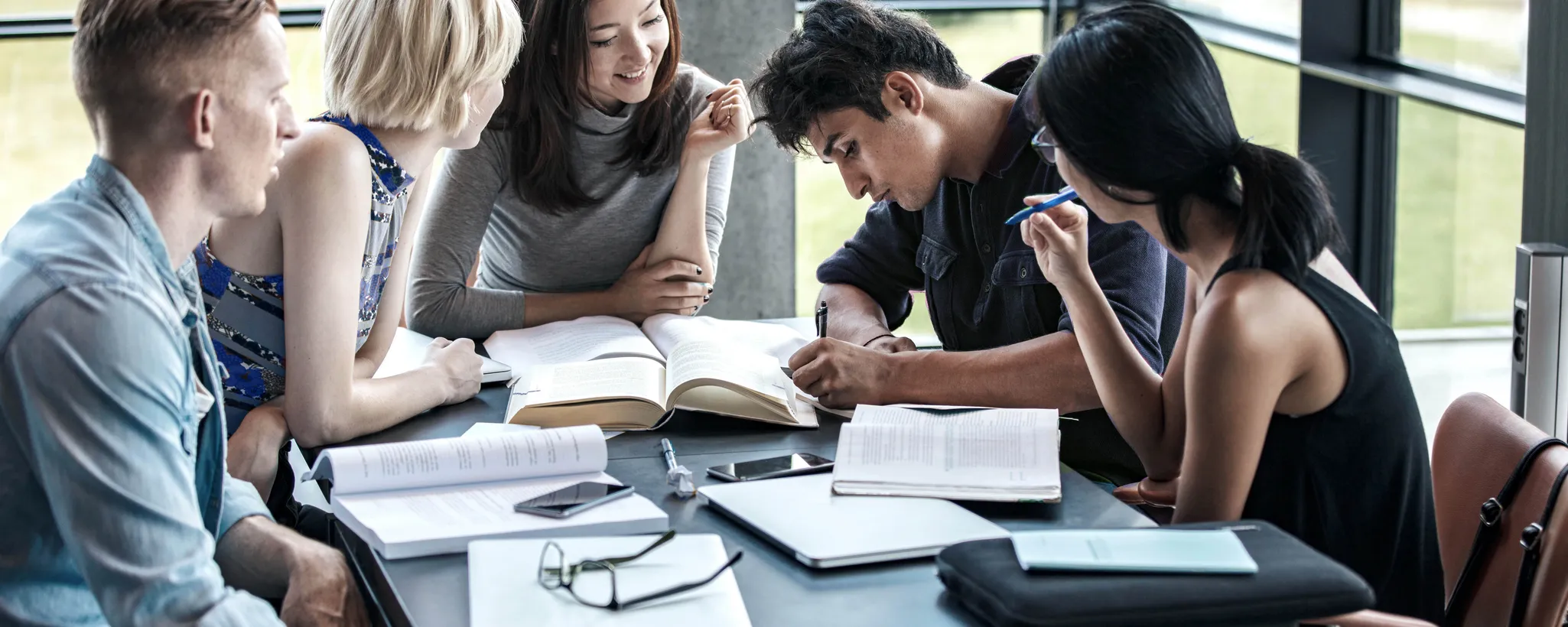Eine Gruppe von Studierenden sitzt an einem Tisch und diskutiert angeregt über Inhalte ihres Versicherung-Studiums. Bücher und Notizen liegen verstreut, während sie sich auf das Versicherung-Studium konzentrieren.