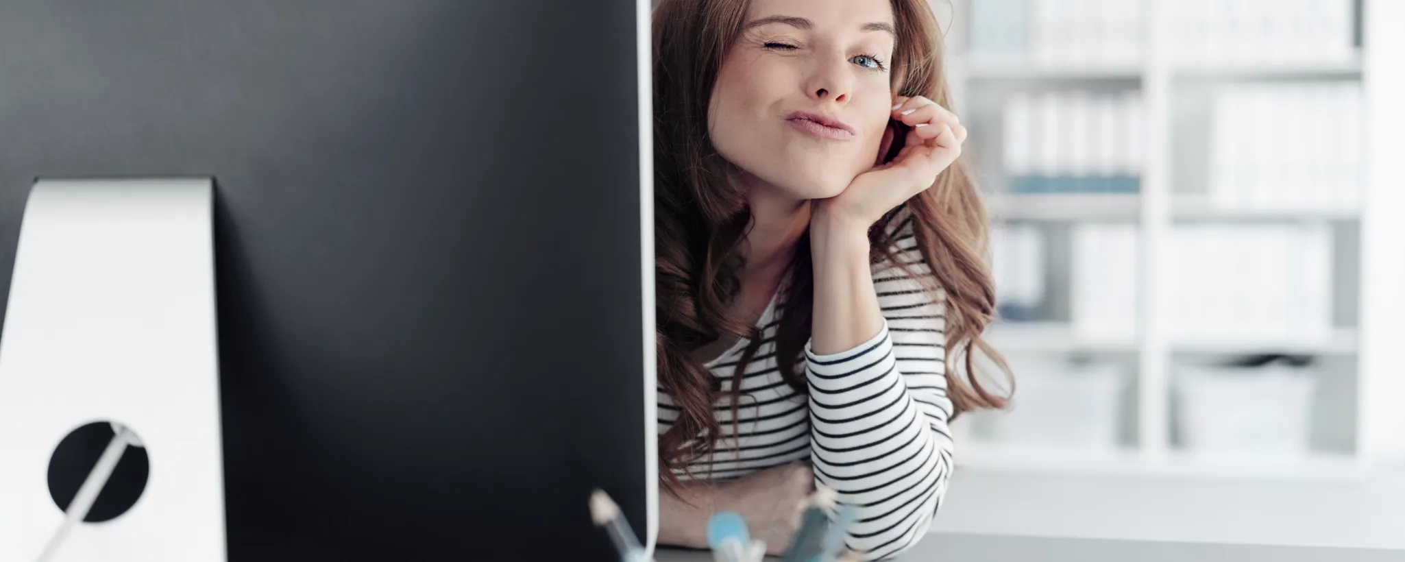 Eine Frau sitzt im Büro vor einem Computer, während sie sich in ihrem Job Alltag mit Dos und Donts auseinandersetzt. Im Hintergrund sind Regale mit Aktenordnern sichtbar.