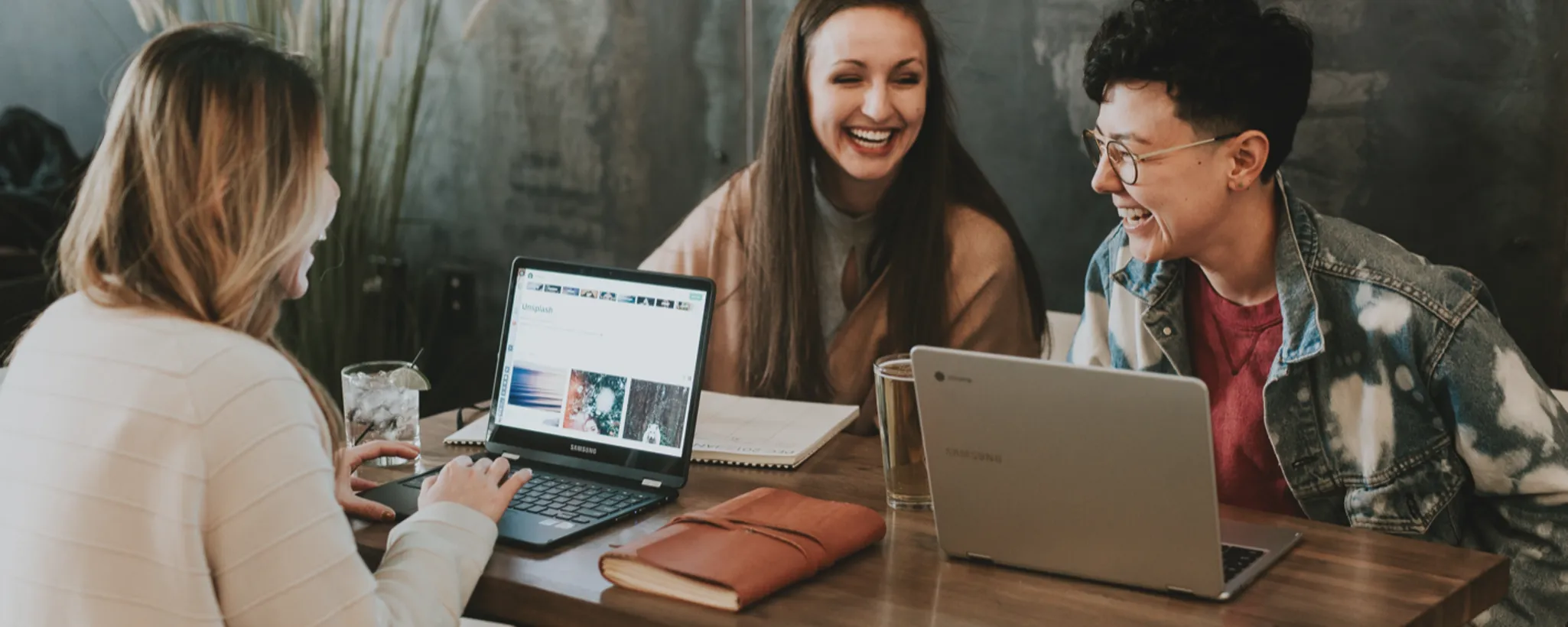 Drei Personen sitzen an einem Tisch in einem Café und arbeiten konzentriert an Laptops. Sie diskutieren angeregt über das Sabbatical, das ihnen kürzlich von ihrem Arbeitgeber angeboten wurde, und tauschen dabei Ideen aus. Neben einem der Laptops liegt ein aufgeschlagenes Notizbuch, in dem wichtige Punkte zum Sabbatical und den Vorschlägen des Arbeitgebers festgehalten werden.