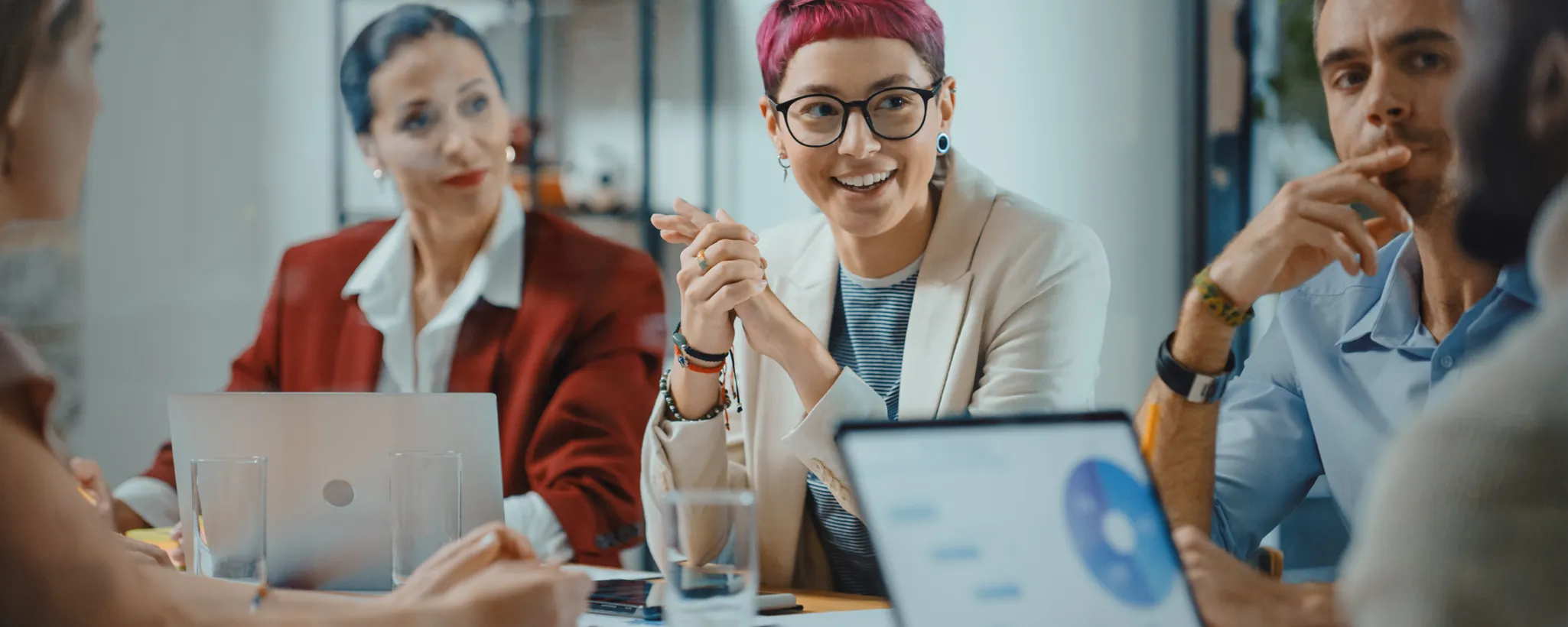 In einem modernen Büro diskutieren mehrere Personen angeregt um einen Tisch, um berufliche Selbstverwirklichung durch innovative Ideen zu fördern, während Laptops und Dokumente ihre Arbeit unterstützen.
