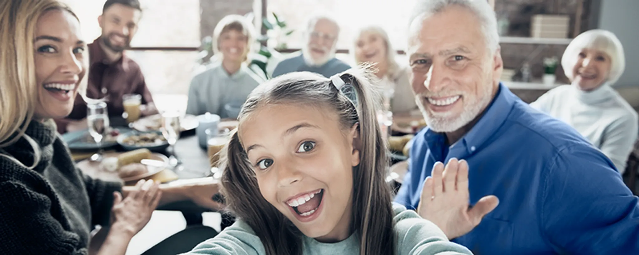 Eine Gruppe von Menschen sitzt rundum einen Tisch, der mit verschiedenen Speisen gedeckt ist. Die Szene vermittelt eine familiäre Atmosphäre, in der sich die Personen über Versicherungen für Familien unterhalten.