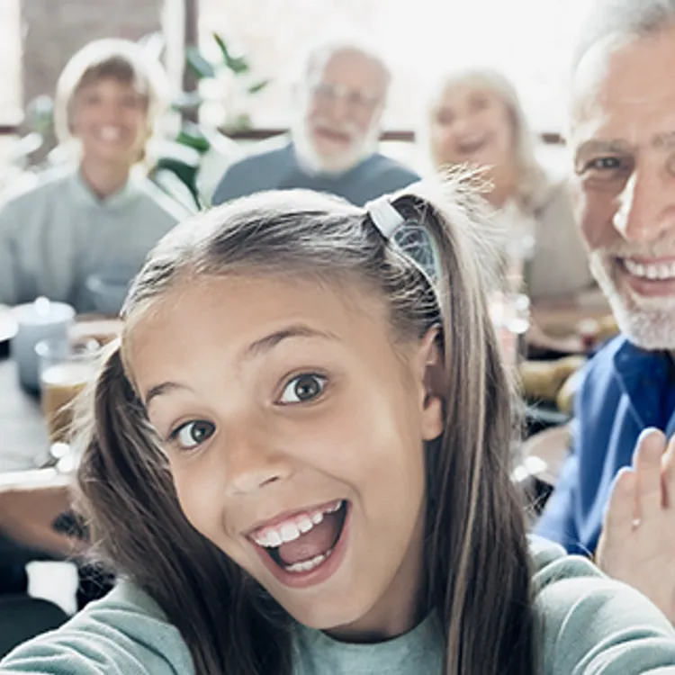 Eine Gruppe von Menschen sitzt rundum einen Tisch, der mit verschiedenen Speisen gedeckt ist. Die Szene vermittelt eine familiäre Atmosphäre, in der sich die Personen über Versicherungen für Familien unterhalten.
