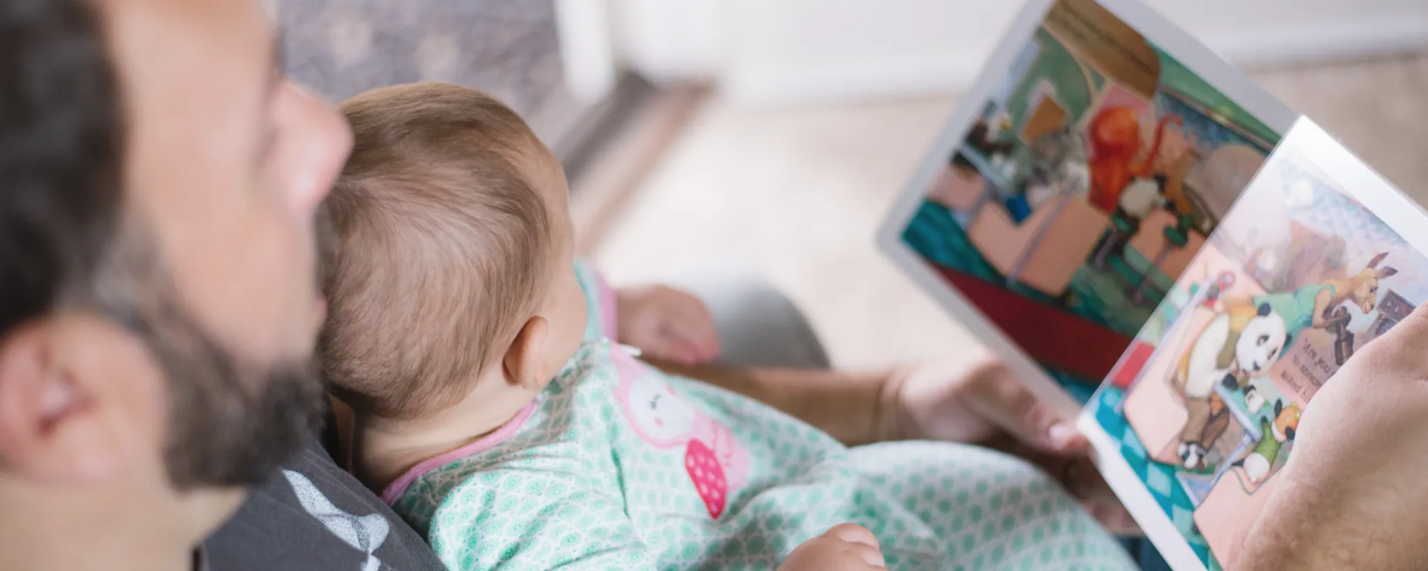 Ein Kleinkind sitzt auf dem Schoß eines Erwachsenen, der ein buntes Bilderbuch hält, während er in der Elternzeit seine Selbstständigkeit genießt.