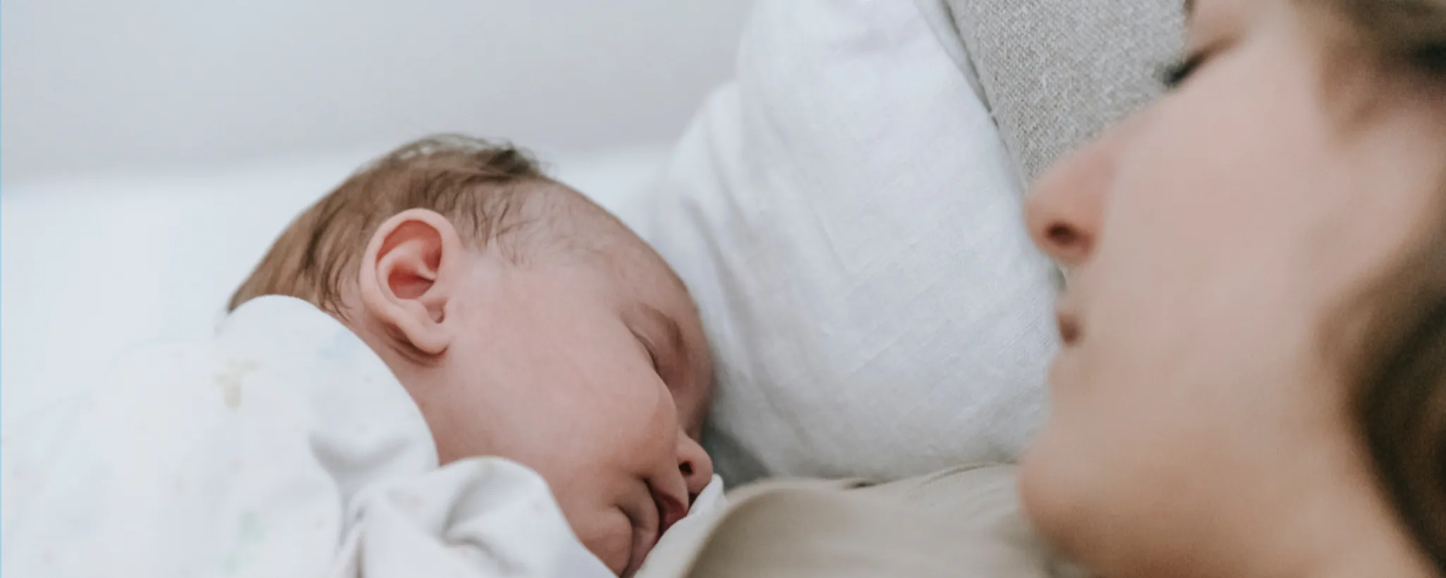 Ein Baby liegt in einem weißen Bett und wird gestillt, während es friedlich ruht. Diese intime Szene spiegelt die Elternzeit in Schweden wider, die Familien unterstützt und ihnen wertvolle gemeinsame Momente während der Elternzeit in Schweden ermöglicht.