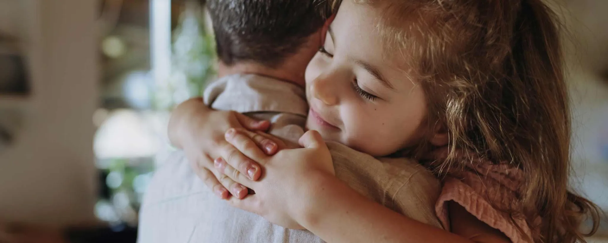 ein Vater hat seine kleine Tochter auf dem Arm umarmt sie herzlich. Er freut sich, dass er für seine Tochter die Kinderabsicherung geregelt hat