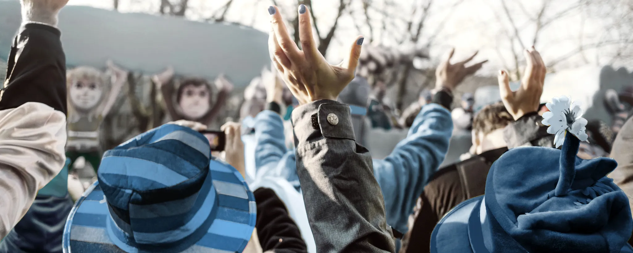 Eine fröhliche Menschenmenge hebt die Hände in die Luft, einige tragen blaue Hüte und Kostüme. Die ausgelassene Stimmung erinnert an einen Karneval, der Spaß und Freude bringt, trotz eines möglichen Unfalltags.