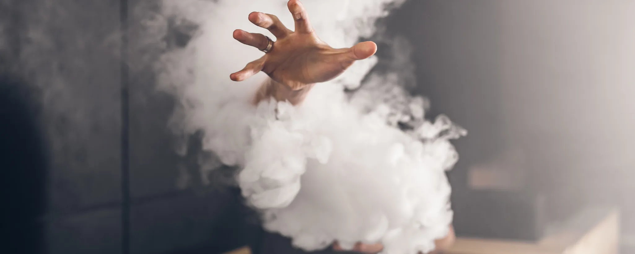 Eine Hand greift durch dichten Rauch, der den Status Quo des Rauchens symbolisiert. Die Szene erinnert an Diskussionen über Gesundheit und Versicherung in Bezug auf Tabakkonsum.