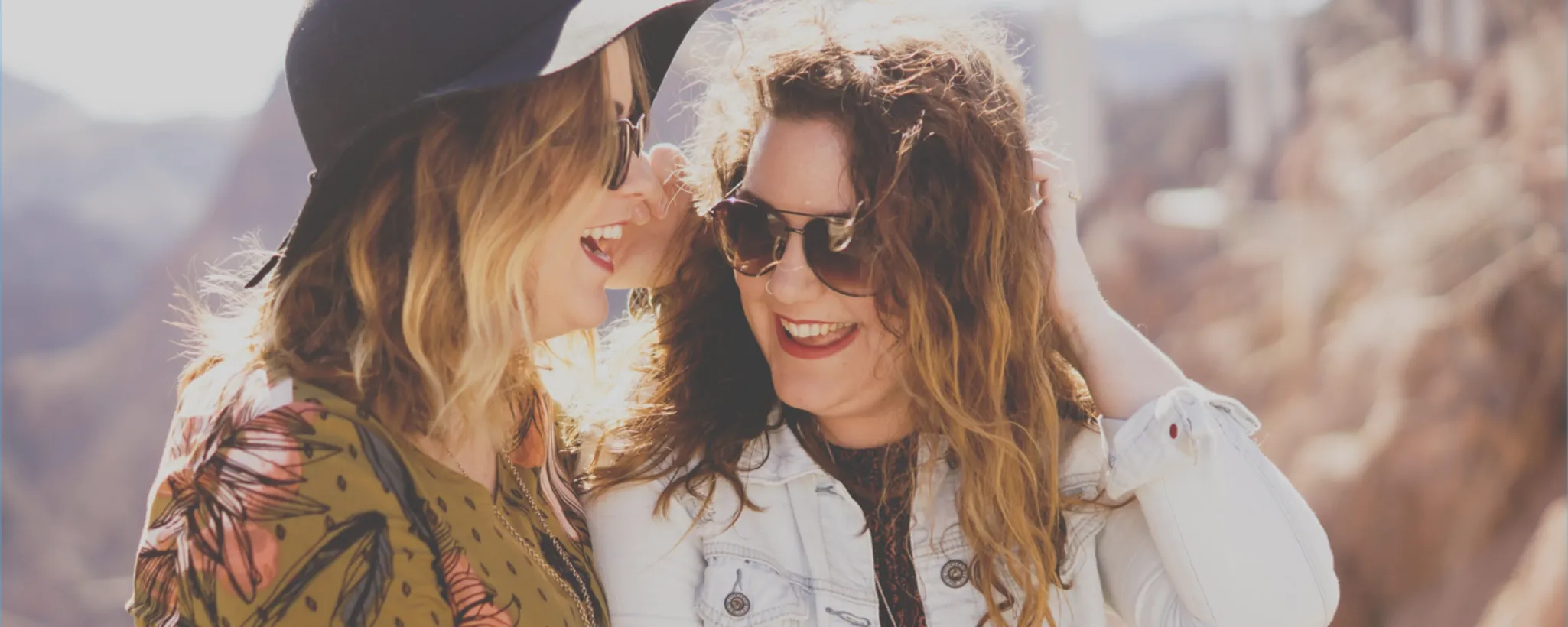 Zwei Frauen stehen in einer sonnigen Landschaft, lachen miteinander und genießen das Zusammensein. Ihre fröhlichen Kontakte tragen zum Wohlbefinden bei und verleihen dem Moment besondere Bedeutung.