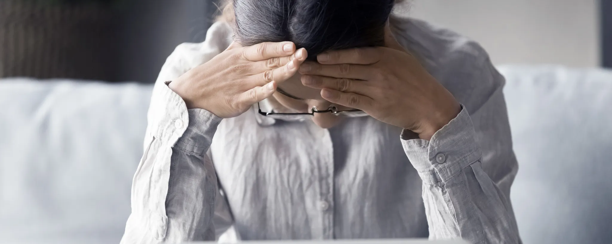 Eine Frau sitzt auf einem Sofa und stützt ihren Kopf in die Hände, offensichtlich erschöpft. Neben ihr liegt ein burnout_e-book, das auf das Thema Stress und Erschöpfung hinweist.