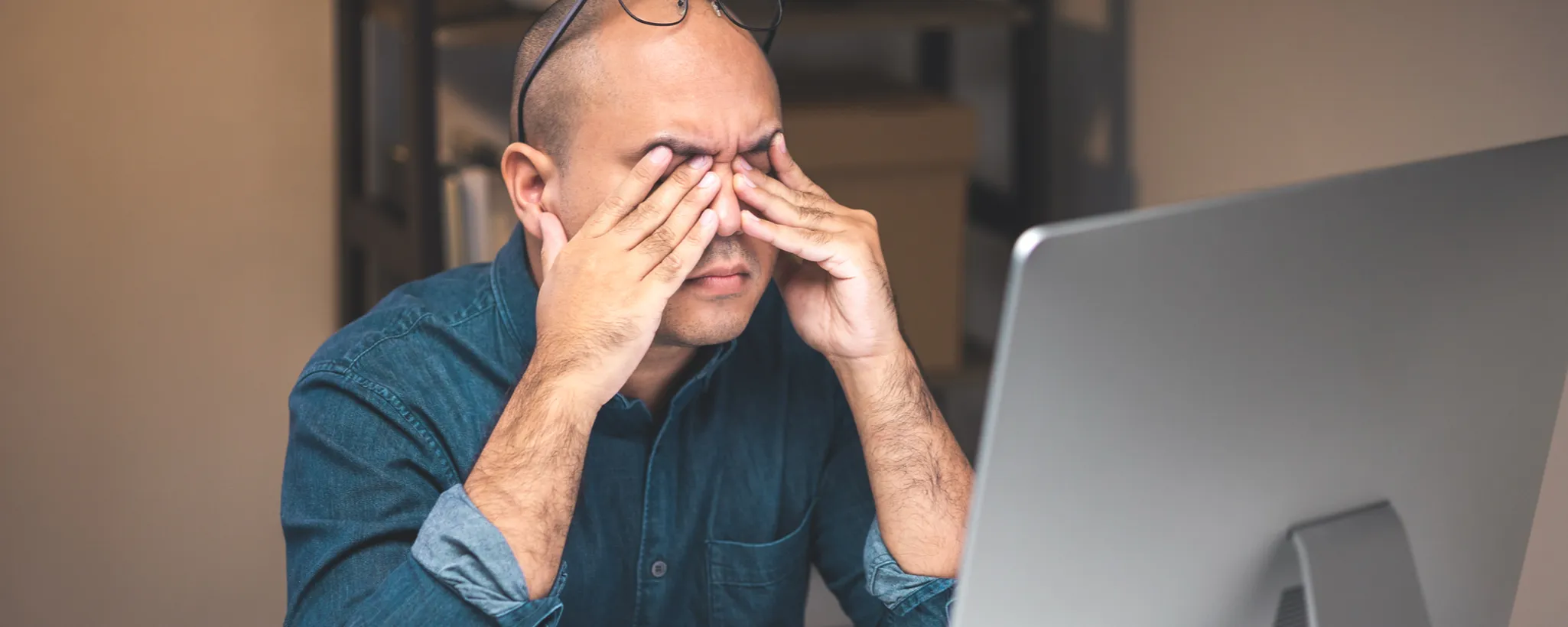Ein Mann sitzt vor dem Bildschirm und reibt sich die Augen. Er zeigt Symptome des Computer-Vision-Syndroms – einer digitalen Augenbelastung, die bei der Arbeit am Bildschirm entstehen kann.
