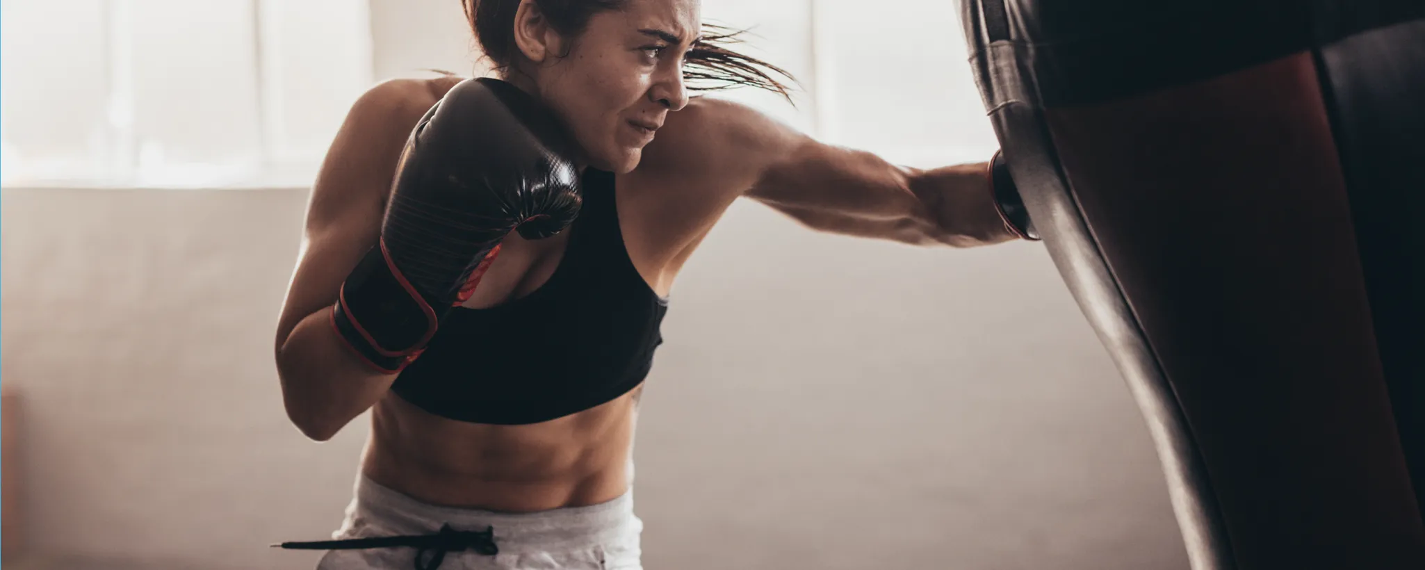 Eine Frau in Sportkleidung trainiert intensiv am Boxsack in einem hellen Raum. Die Szene vermittelt den Leistungsdruck, den viele am Arbeitsplatz empfinden, durch körperliche Aktivität.