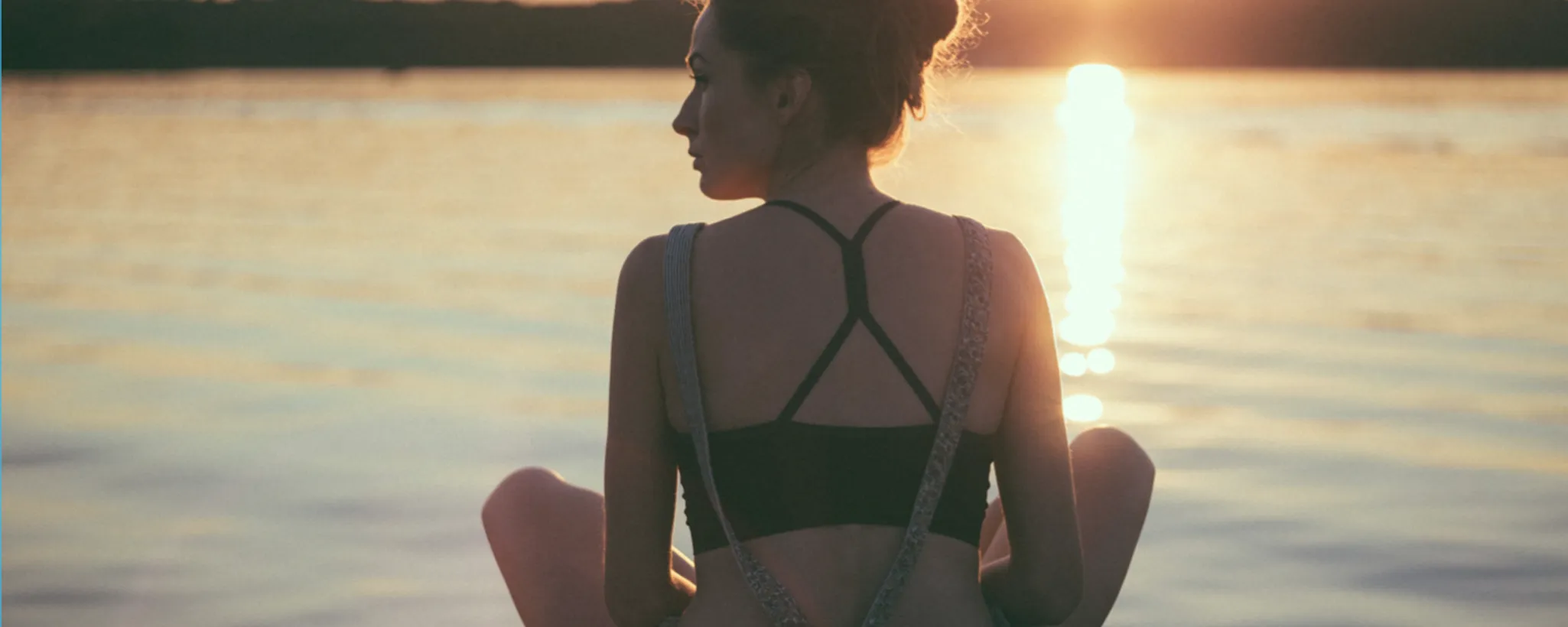 Eine Person sitzt meditativ am Ufer eines Sees, während die Sonne untergeht. In der Ruhe dieses Moments wird der Stress des Alltags, oft Auslöser von Volkskrankheiten, vergessen.