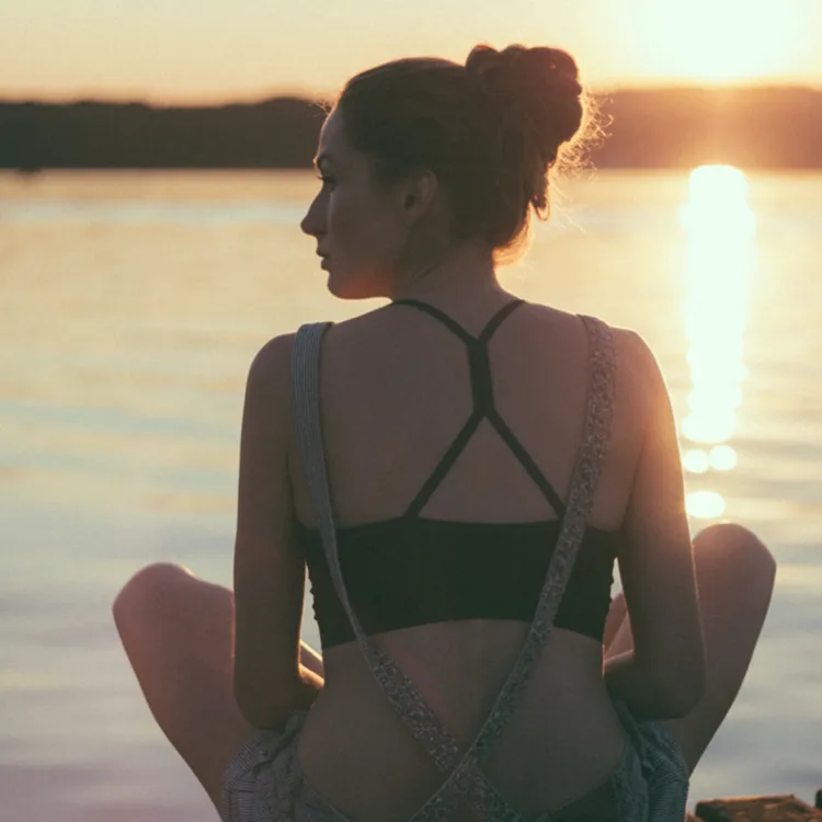 Eine Person sitzt meditativ am Ufer eines Sees, während die Sonne untergeht. In der Ruhe dieses Moments wird der Stress des Alltags, oft Auslöser von Volkskrankheiten, vergessen.