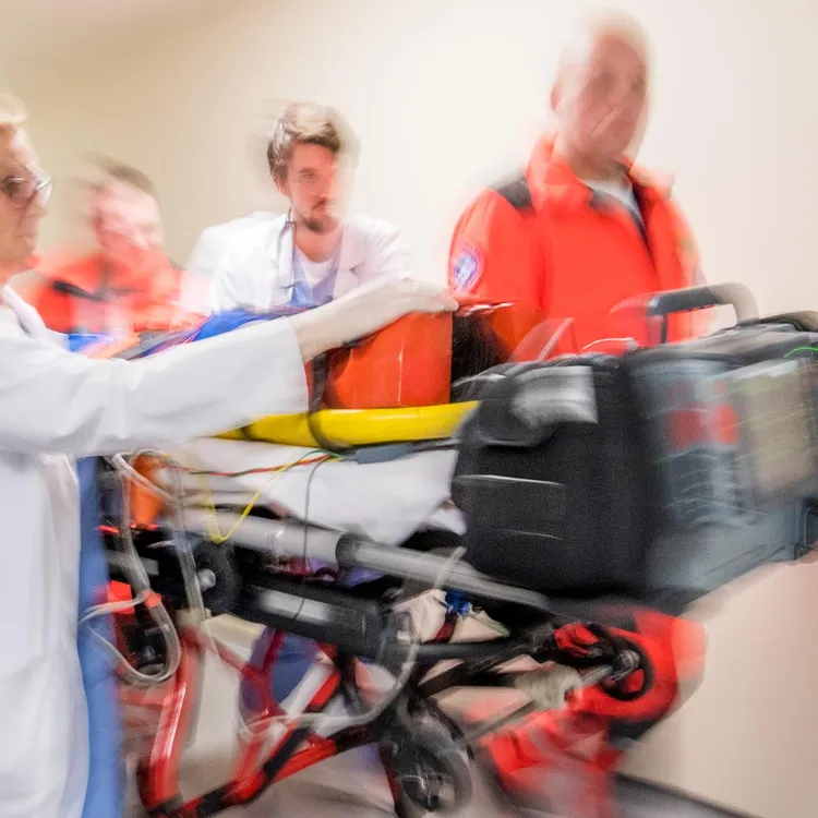 Im Krankenhausflur eilen Notärzte bei ihrer Arbeit mit einer Trage, auf der ein Patient liegt, durch den Gang. Die Szene vermittelt Dringlichkeit und Professionalität.