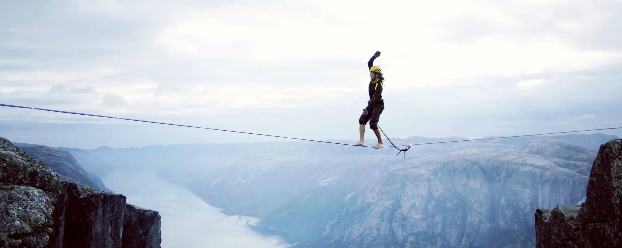 Auf einem Seil balanciert eine Frau zwischen zwei Bergen über eine Klippe