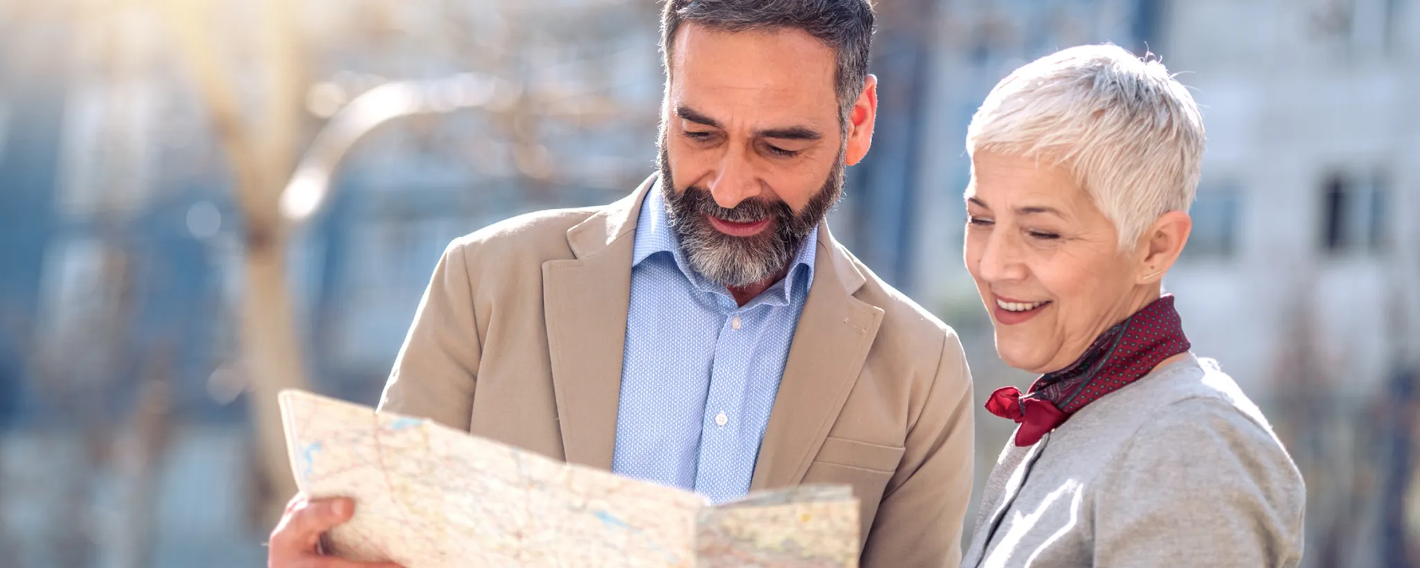 Zwei Senioren stehen im Freien und betrachten gemeinsam eine große Landkarte. Sie sind warm gekleidet und die Sonne scheint auf sie, was eine entspannte Atmosphäre schafft, die an die Sicherheit einer Lebensversicherung erinnert.