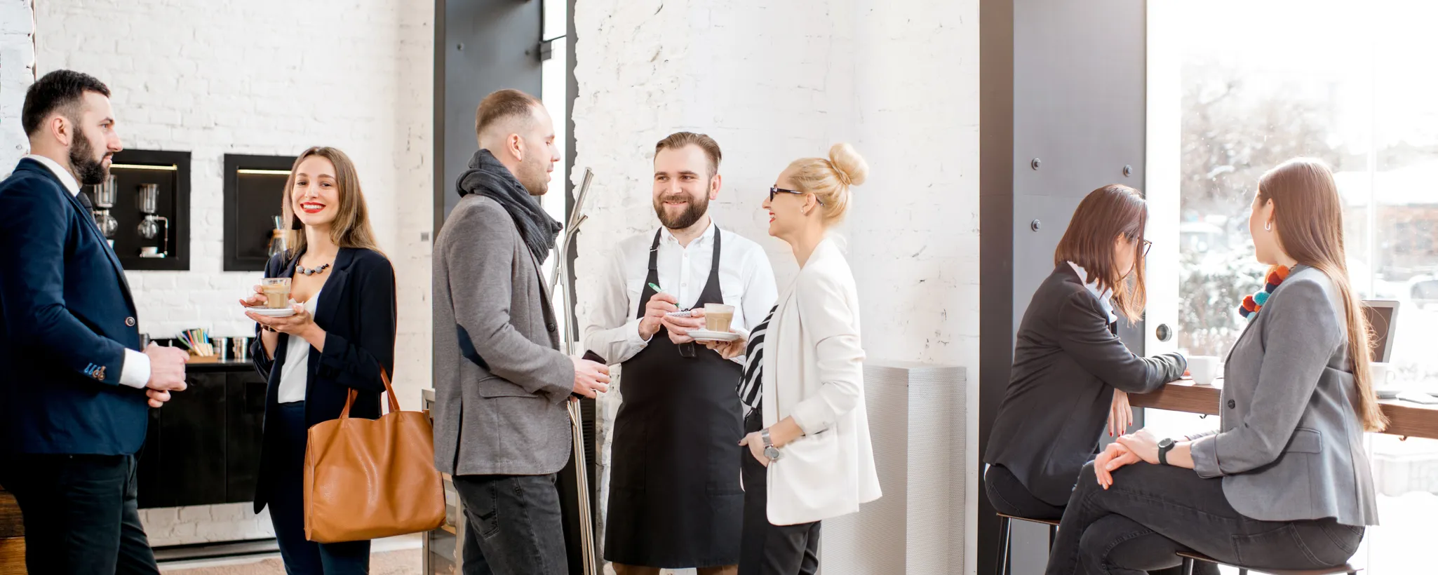 In einem modernen Café stehen mehrere Personen in Geschäftskleidung, während ein Kellner Bestellungen aufnimmt. Sie diskutieren angeregt über Neuerungen in der betrieblichen Altersvorsorge. Dabei liegt der Fokus auf den Vorteilen und Herausforderungen, die mit der betrieblichen Altersvorsorge verbunden sind, und wie diese sich auf die finanzielle Sicherheit im Alter auswirken können.