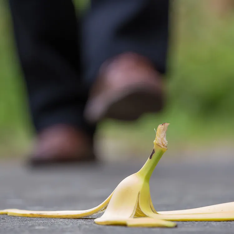 Ein Schuh nähert sich einer auf dem Boden liegenden Bananenschale, eine klassische Besonderheit, die oft mit der Notwendigkeit einer Unfallversicherung in Verbindung gebracht wird.