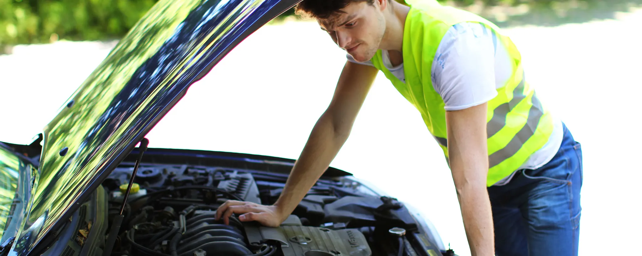 Eine Person steht neben einem geöffneten Auto und trägt eine gelbe Warnweste, die in Deutschland bei Pannen vorgeschrieben ist, um die Sichtbarkeit zu erhöhen.