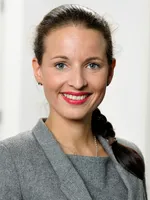 Sina Rintelmann, die als Datenschutzbeauftragte tätig ist, trägt einen grauen Blazer und hat ihr dunkles Haar zu einem Zopf gebunden. Ein dezenter Hintergrund ergänzt das professionelle Erscheinungsbild.