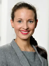 Sina Rintelmann, die als Datenschutzbeauftragte tätig ist, trägt einen grauen Blazer und hat ihr dunkles Haar zu einem Zopf gebunden. Ein dezenter Hintergrund ergänzt das professionelle Erscheinungsbild.