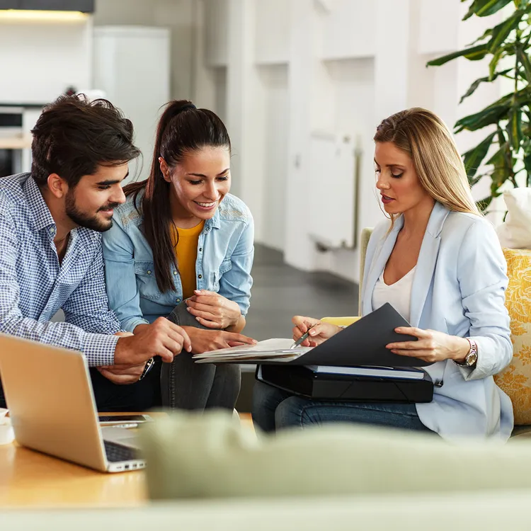 In einem modernen Büro bespricht eine Beraterin mit zwei Personen Unterlagen. Sie bietet persönliche Beratung zu Direktversicherern an, während ein Laptop auf dem Tisch steht.