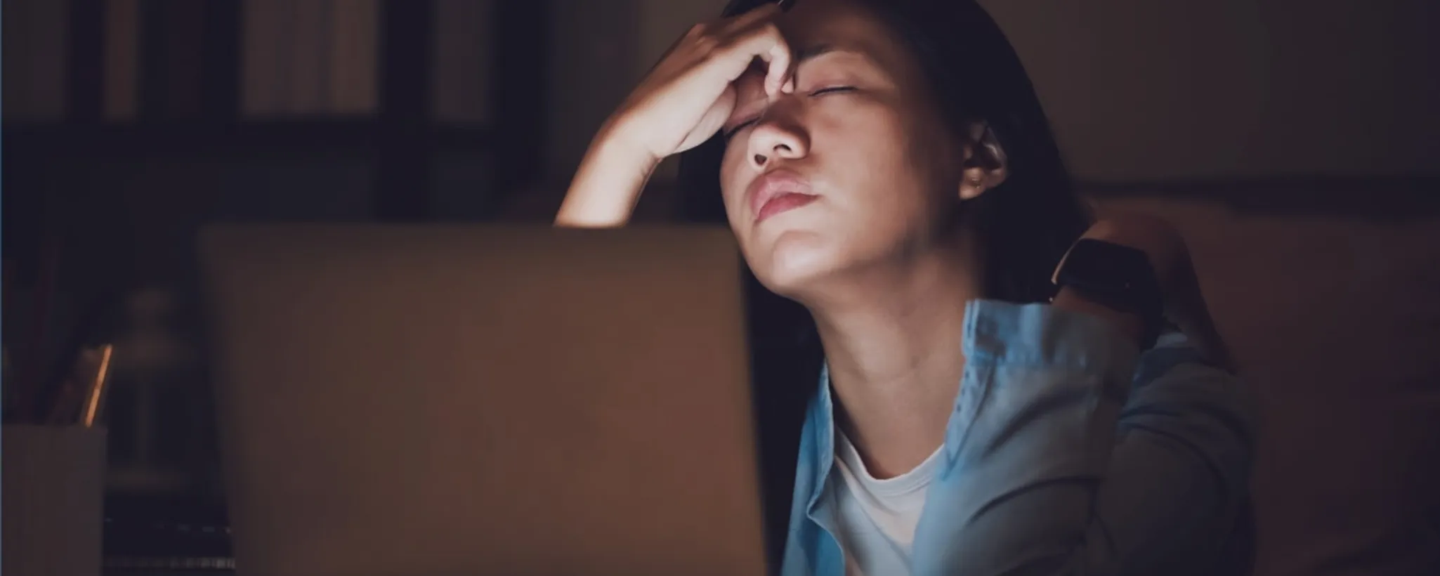 Eine Person sitzt spätabends vor einem Laptop, während sie nachdenklich ihren Kopf stützt. Im Hintergrund sind Bücherregale zu sehen, die eine ruhige, konzentrierte Arbeitsatmosphäre schaffen, wie man sie oft in Versicherungsgesellschaften findet.